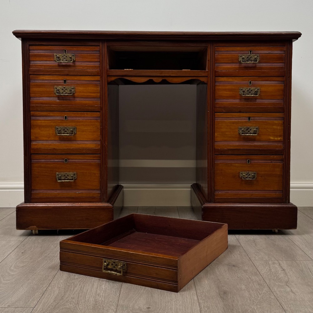 An Edwardian mahogany pedestal desk featuring nine reeded drawers with decorative brass drop handles and a central kneehole. View X