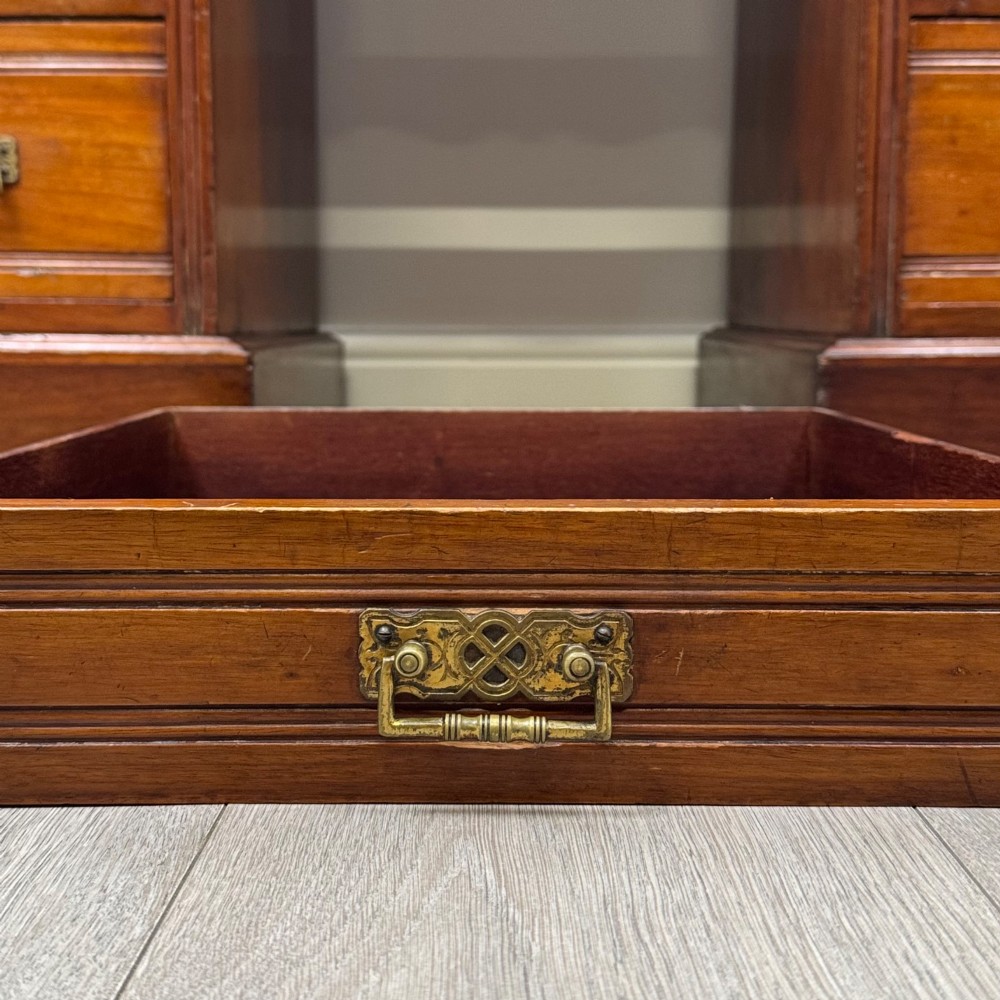 An Edwardian mahogany pedestal desk featuring nine reeded drawers with decorative brass drop handles and a central kneehole. View XI