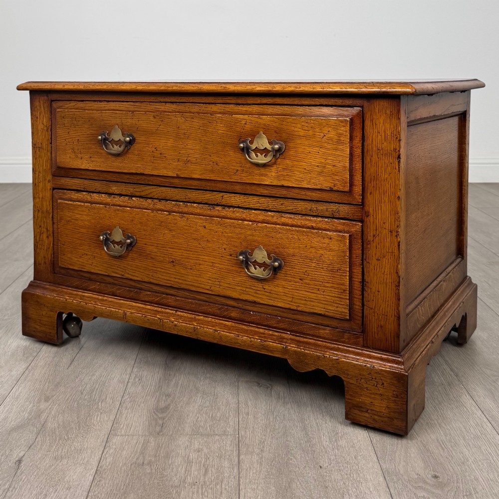 A low two-drawer oak chest featuring raised panel fronts, decorative brass drop handles, and bracket feet in a warm brown finish. View III