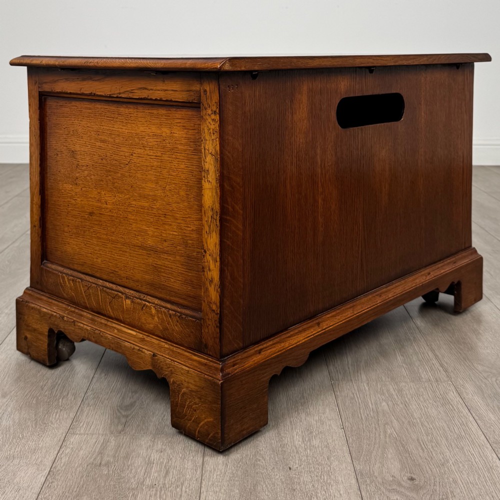 A low two-drawer oak chest featuring raised panel fronts, decorative brass drop handles, and bracket feet in a warm brown finish. View V