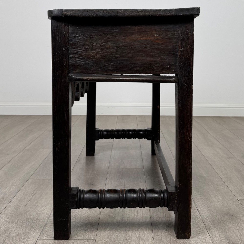 A dark oak 19th-century side table featuring floral relief carvings on two drawer fronts, a row of carved cusped arches along the lower apron, and turned side stretchers. View III