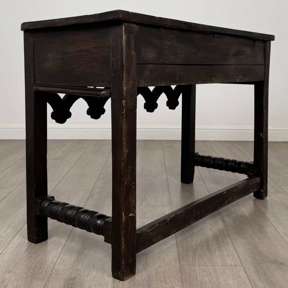 A dark oak 19th-century side table featuring floral relief carvings on two drawer fronts, a row of carved cusped arches along the lower apron, and turned side stretchers. View IV
