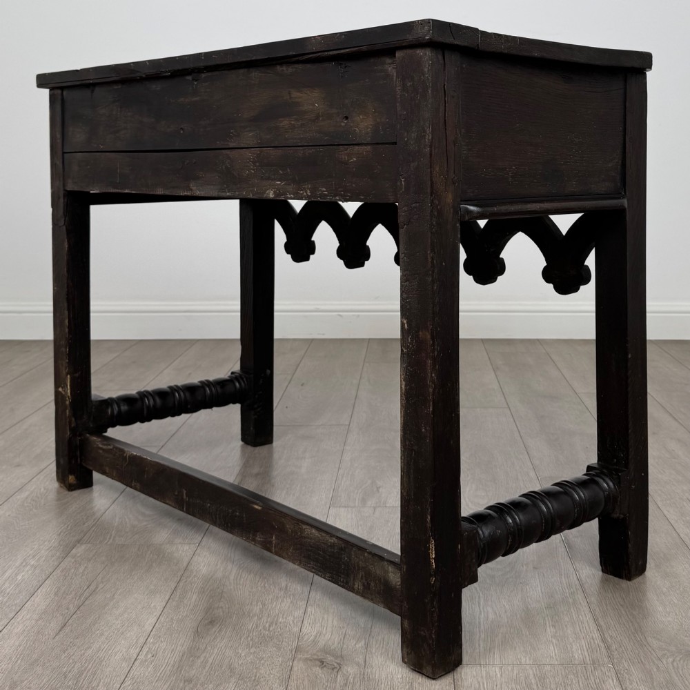 A dark oak 19th-century side table featuring floral relief carvings on two drawer fronts, a row of carved cusped arches along the lower apron, and turned side stretchers. View VI