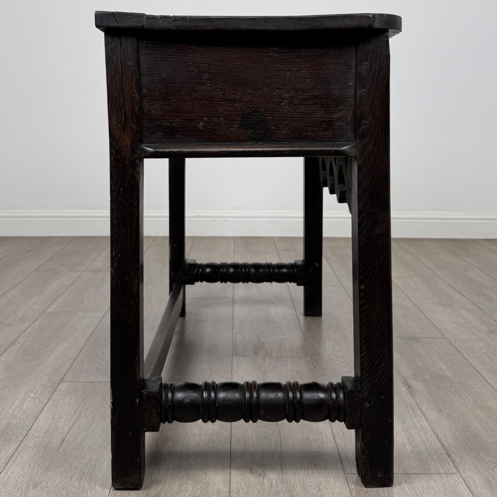 A dark oak 19th-century side table featuring floral relief carvings on two drawer fronts, a row of carved cusped arches along the lower apron, and turned side stretchers. View VII