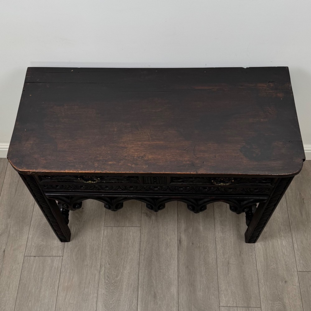A dark oak 19th-century side table featuring floral relief carvings on two drawer fronts, a row of carved cusped arches along the lower apron, and turned side stretchers. View IX
