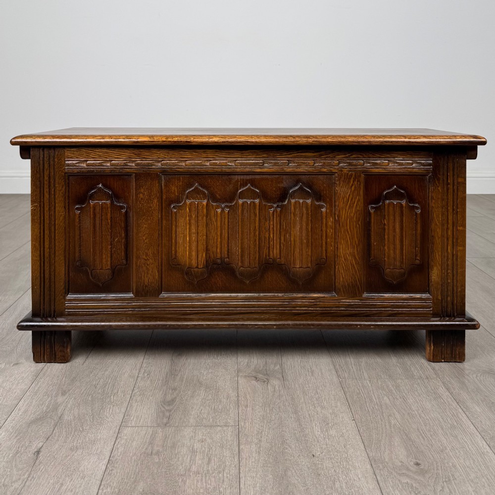 A rectangular dark oak blanket box featuring three carved front panels with Gothic arched details and a flat top lid.