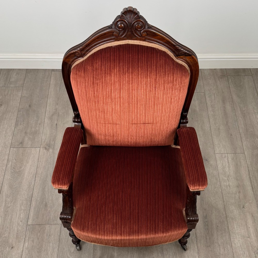 A Victorian rosewood armchair featuring a dark timber frame, carved scroll detailing, rust red velvet upholstery, and turned front legs on castors. View XIII