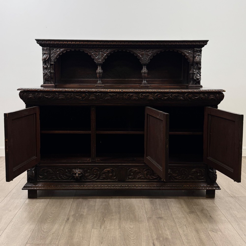 A dark oak 19th-century sideboard featuring deep relief carvings of Green Man mythical faces, foliate motifs, lion masks, and an arched upper gallery shelf. View II