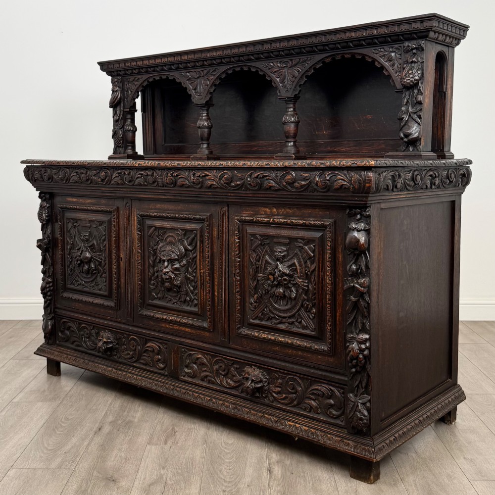 A dark oak 19th-century sideboard featuring deep relief carvings of Green Man mythical faces, foliate motifs, lion masks, and an arched upper gallery shelf. View III