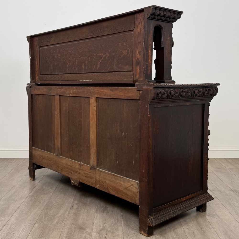 A dark oak 19th-century sideboard featuring deep relief carvings of Green Man mythical faces, foliate motifs, lion masks, and an arched upper gallery shelf. View VII