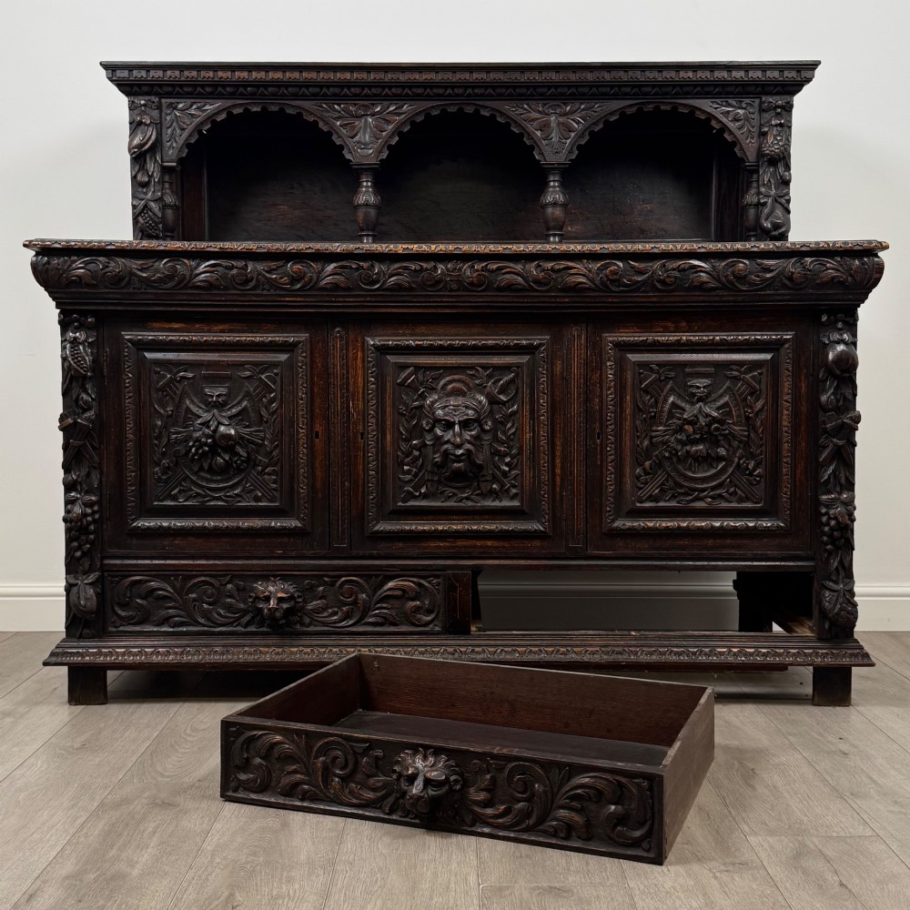 A dark oak 19th-century sideboard featuring deep relief carvings of Green Man mythical faces, foliate motifs, lion masks, and an arched upper gallery shelf. View XI