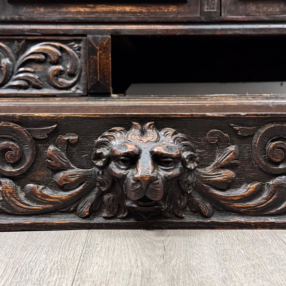 A dark oak 19th-century sideboard featuring deep relief carvings of Green Man mythical faces, foliate motifs, lion masks, and an arched upper gallery shelf. View XII