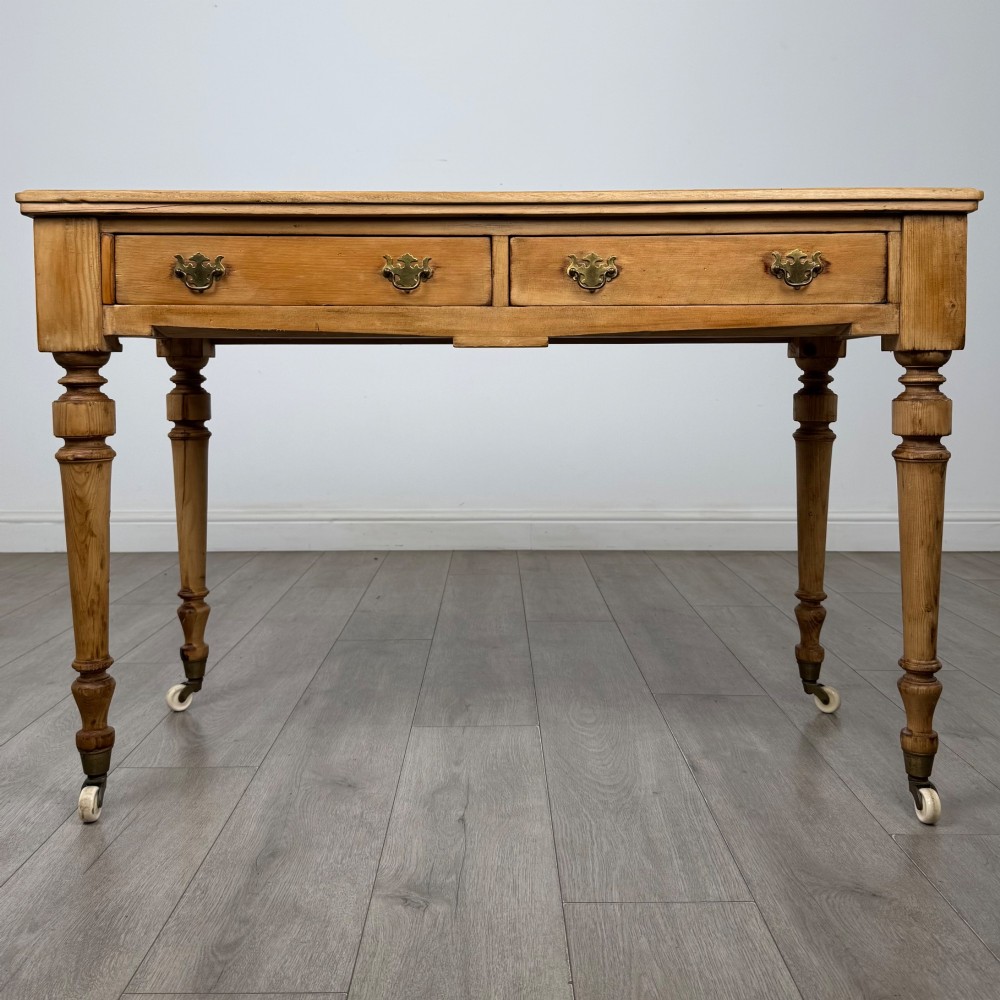A 19th-century Victorian pine writing table featuring two drawers with brass handles, turned wooden legs, and ceramic castors.