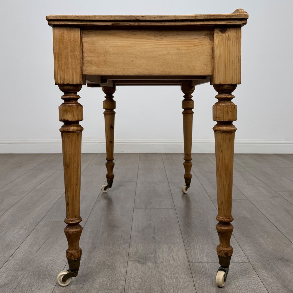 A 19th-century Victorian pine writing table featuring two drawers with brass handles, turned wooden legs, and ceramic castors. View III