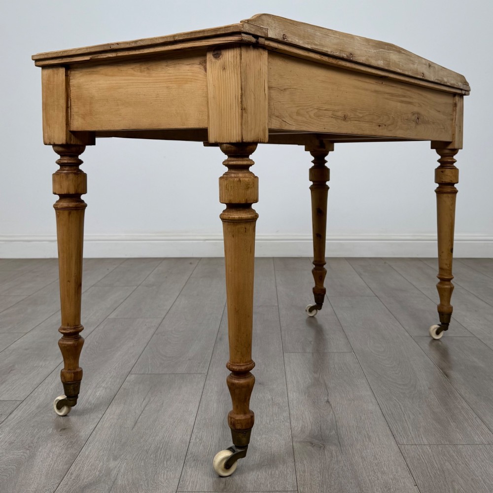 A 19th-century Victorian pine writing table featuring two drawers with brass handles, turned wooden legs, and ceramic castors. View IV