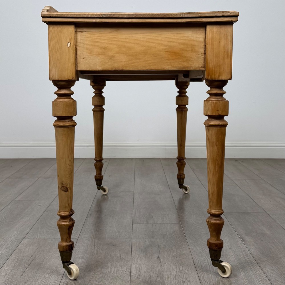 A 19th-century Victorian pine writing table featuring two drawers with brass handles, turned wooden legs, and ceramic castors. View VII