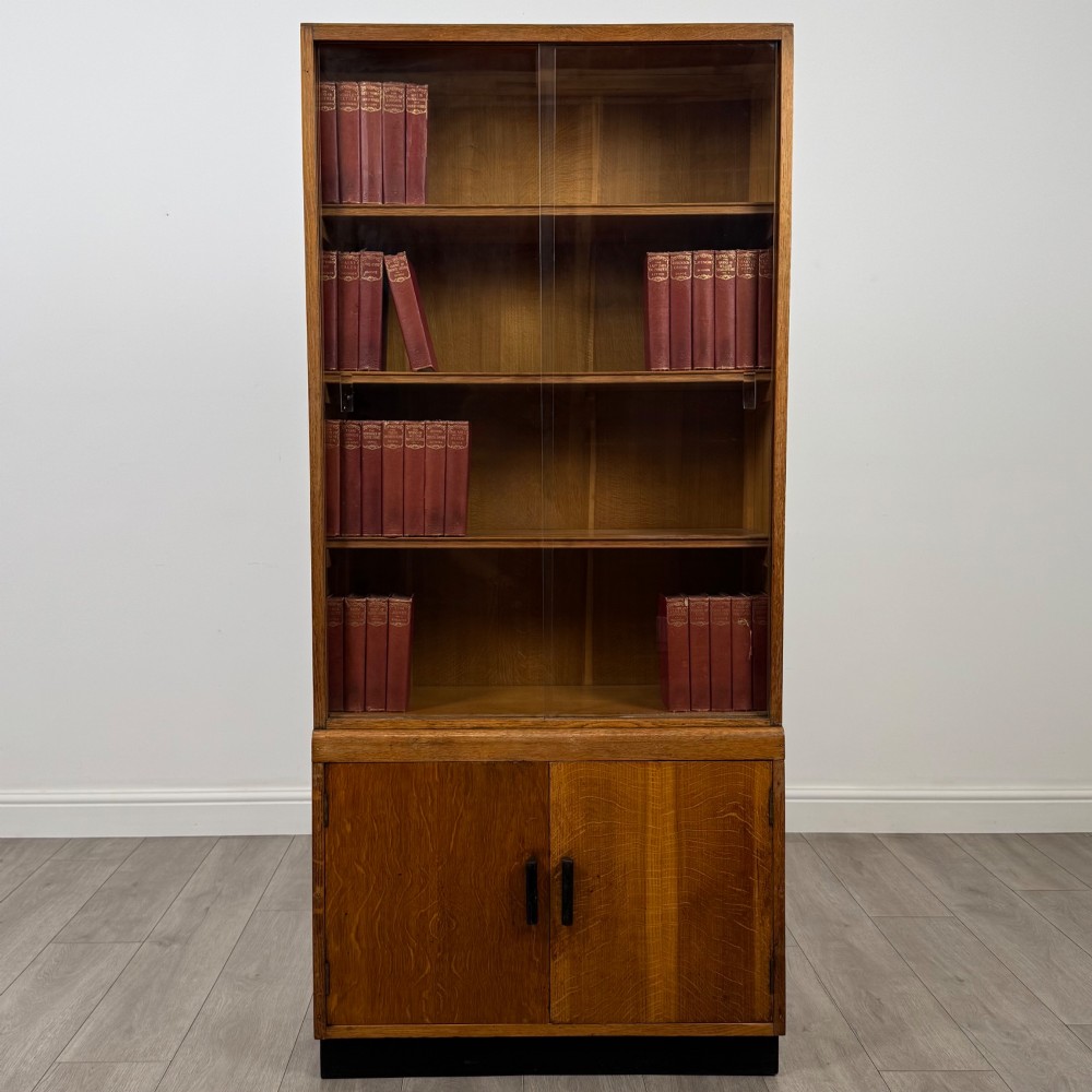 A tall vintage golden oak display cabinet featuring glazed sliding doors on top and a two-door cupboard base.
