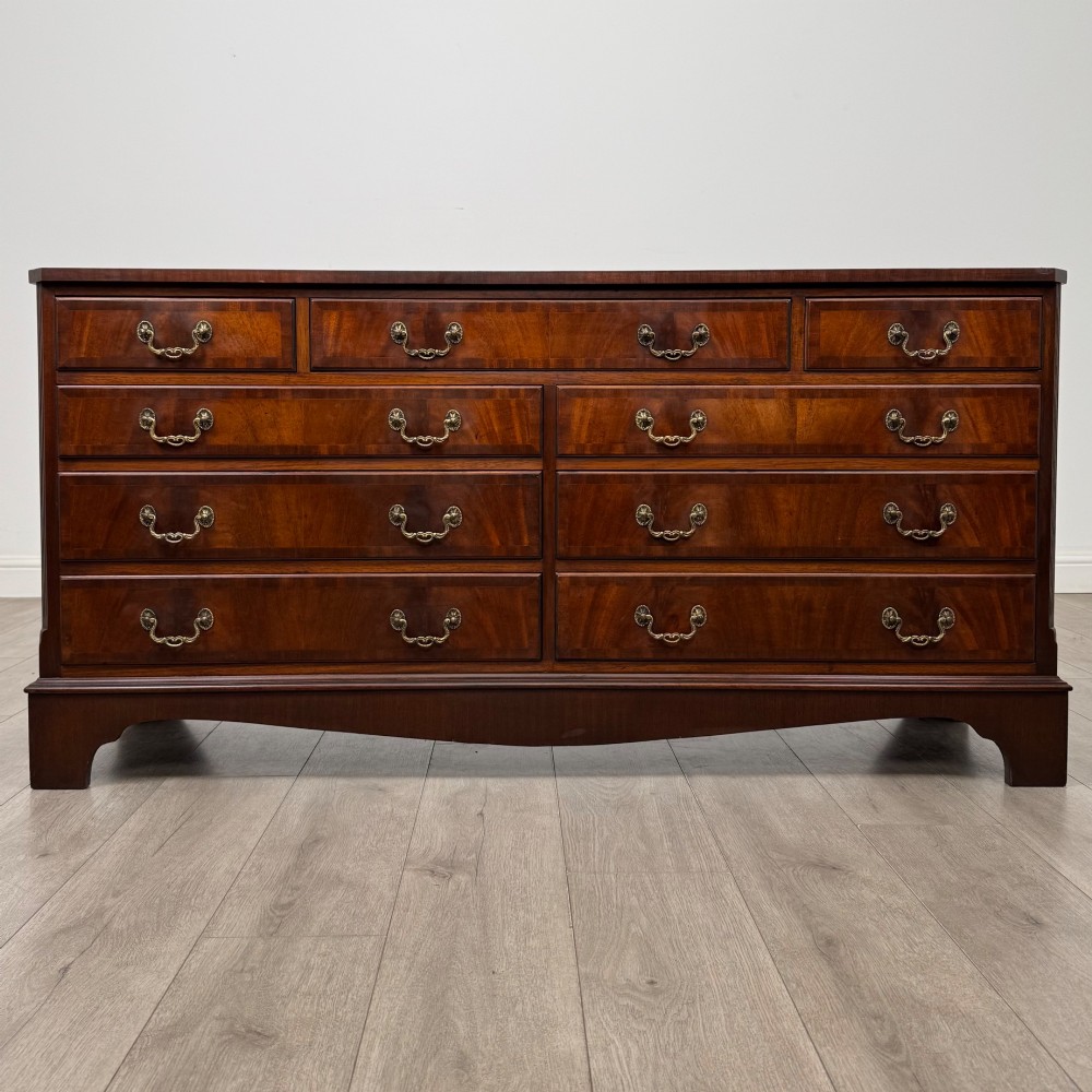 A wide 20th-century mahogany chest of drawers featuring multiple drawer tiers with flame mahogany veneer and decorative brass handles.