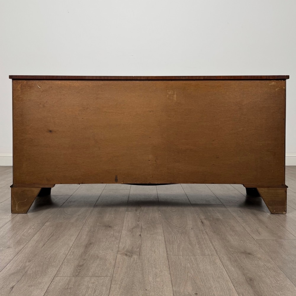 A wide 20th-century mahogany chest of drawers featuring multiple drawer tiers with flame mahogany veneer and decorative brass handles. View V