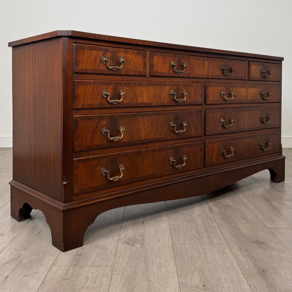 A wide 20th-century mahogany chest of drawers featuring multiple drawer tiers with flame mahogany veneer and decorative brass handles. View VIII