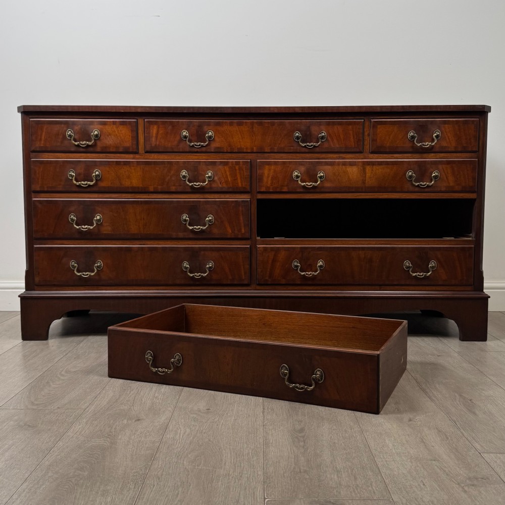 A wide 20th-century mahogany chest of drawers featuring multiple drawer tiers with flame mahogany veneer and decorative brass handles. View X