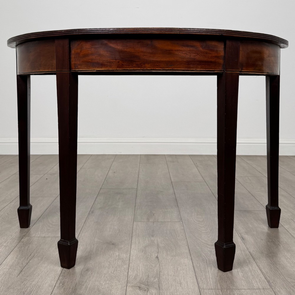 A nineteenth-century mahogany demi-lune side table featuring a semi-circular top, a veneered apron, and four square tapered legs ending in spade feet.