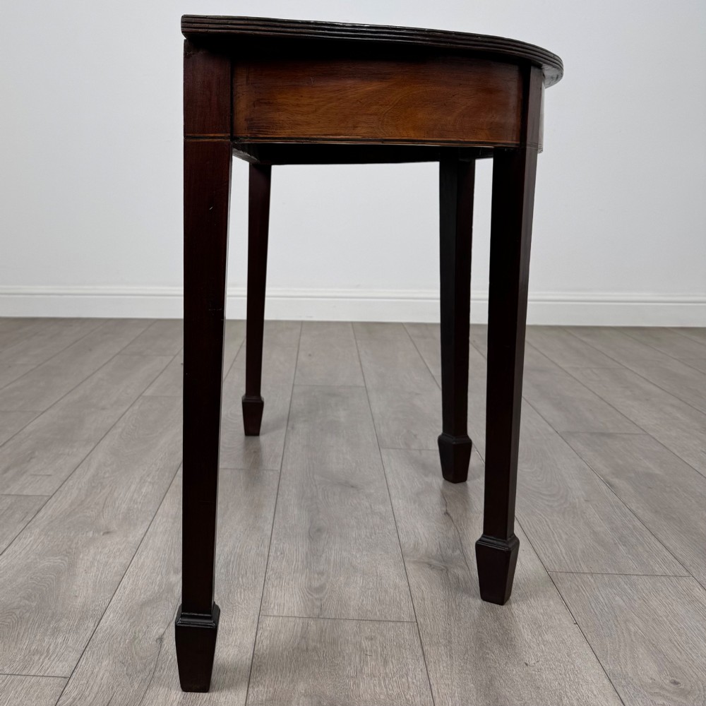 A nineteenth-century mahogany demi-lune side table featuring a semi-circular top, a veneered apron, and four square tapered legs ending in spade feet. View V