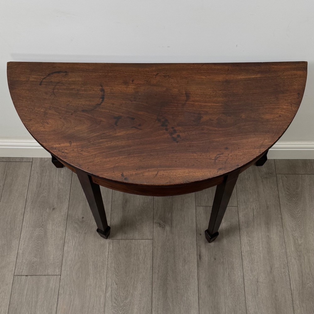 A nineteenth-century mahogany demi-lune side table featuring a semi-circular top, a veneered apron, and four square tapered legs ending in spade feet. View VII