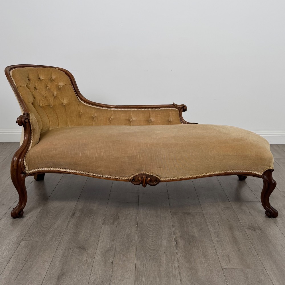 A Victorian mahogany chaise longue featuring ochre velvet button-backed upholstery, carved trim, and cabriole legs.