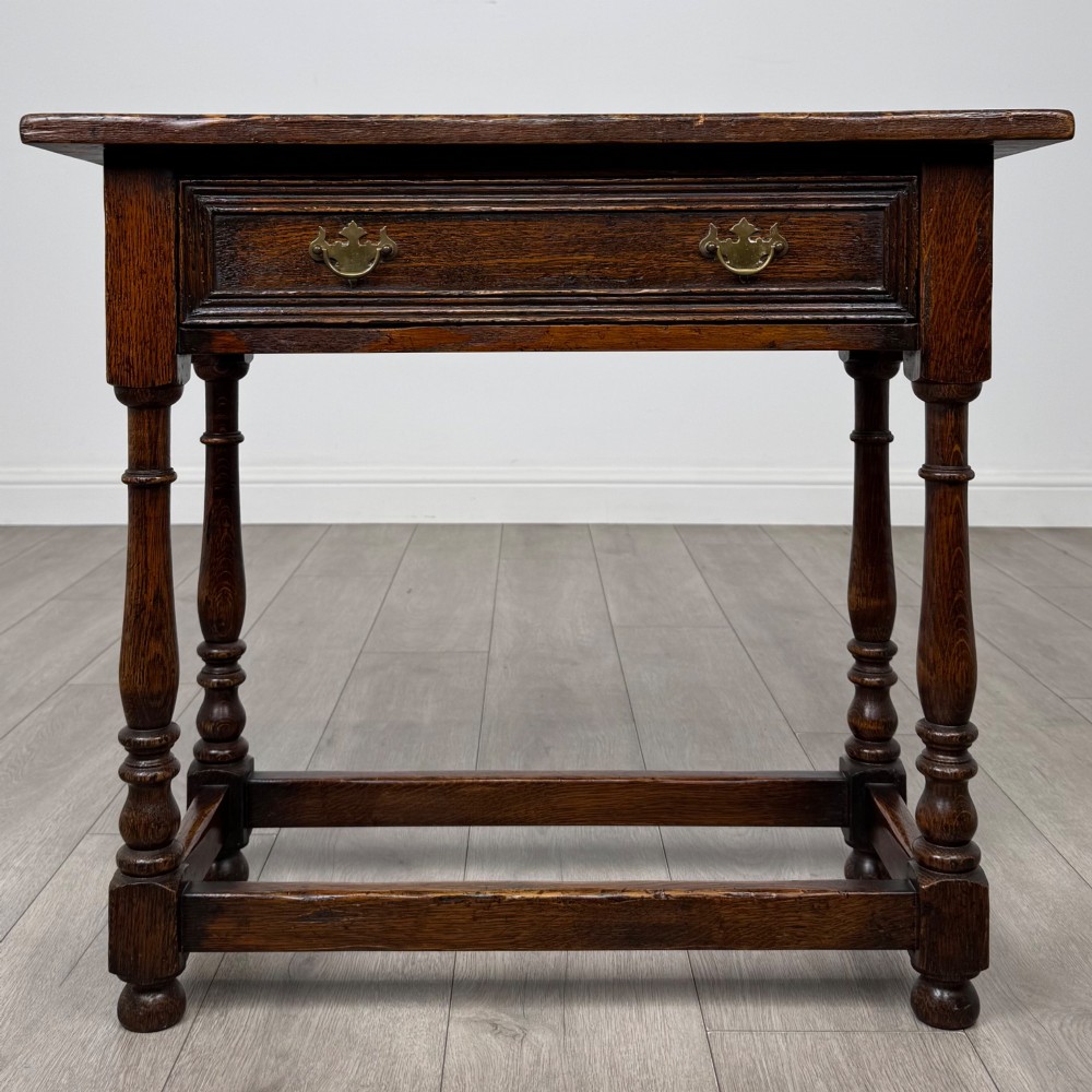 A dark oak side table featuring a single drawer with brass drop handles, turned legs, and a perimeter box stretcher.