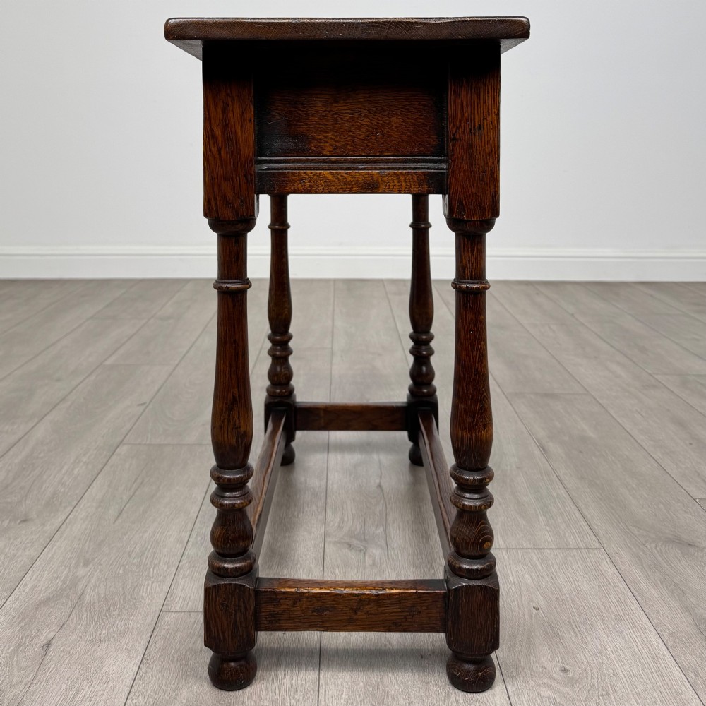 A dark oak side table featuring a single drawer with brass drop handles, turned legs, and a perimeter box stretcher. View III