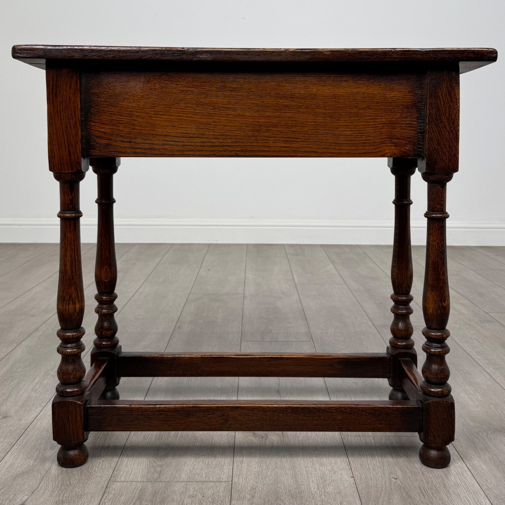 A dark oak side table featuring a single drawer with brass drop handles, turned legs, and a perimeter box stretcher. View V