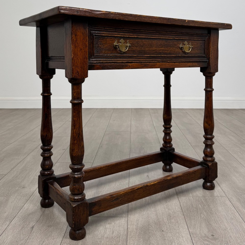 A dark oak side table featuring a single drawer with brass drop handles, turned legs, and a perimeter box stretcher. View VIII