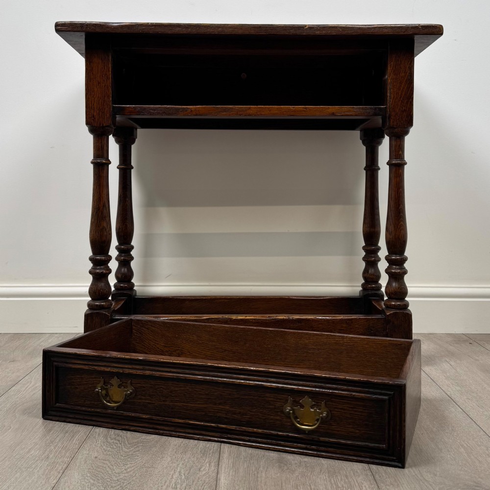 A dark oak side table featuring a single drawer with brass drop handles, turned legs, and a perimeter box stretcher. View X