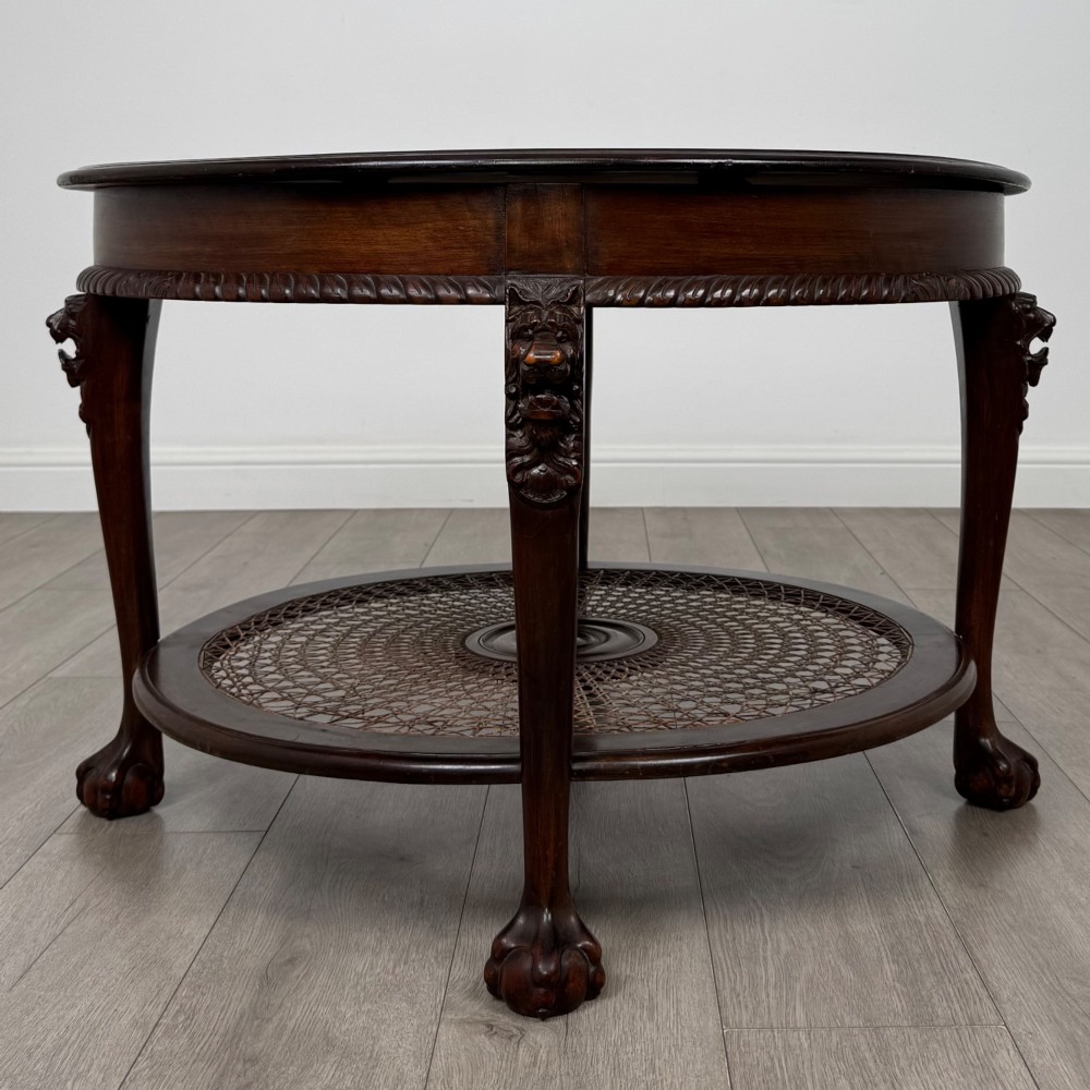 A circular dark mahogany coffee table featuring carved lion heads atop cabriole legs ending in claw and ball feet, with a woven cane lower shelf. View II
