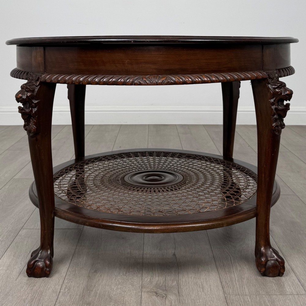 A circular dark mahogany coffee table featuring carved lion heads atop cabriole legs ending in claw and ball feet, with a woven cane lower shelf. View III