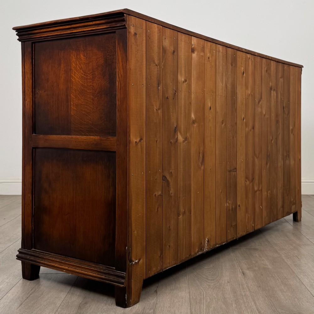 A twentieth-century warm oak sideboard featuring three upper drawers with brass handles above three cupboard doors decorated with geometric moulded panels and exterior brass H-hinges. View V