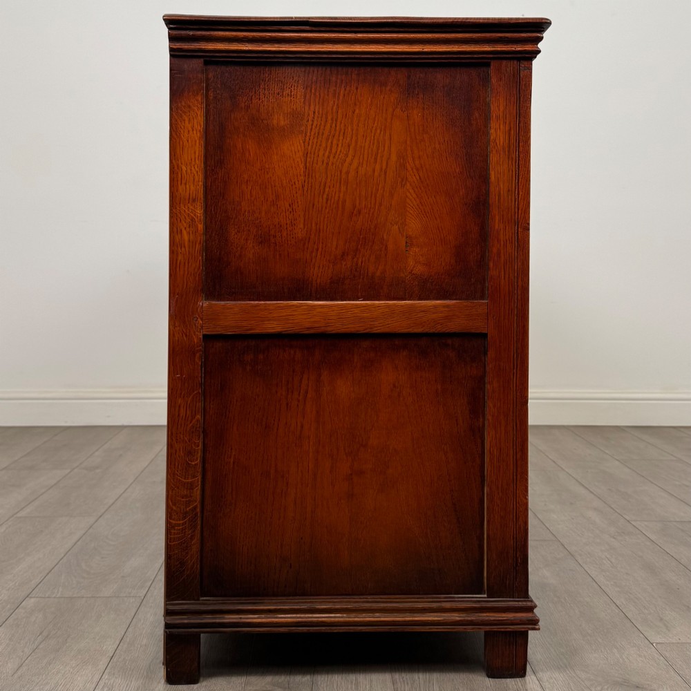 A twentieth-century warm oak sideboard featuring three upper drawers with brass handles above three cupboard doors decorated with geometric moulded panels and exterior brass H-hinges. View VIII