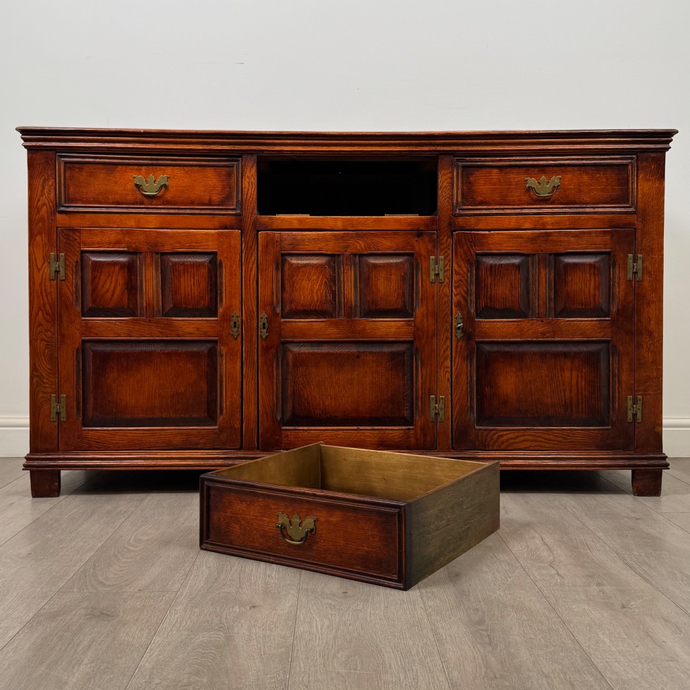 A twentieth-century warm oak sideboard featuring three upper drawers with brass handles above three cupboard doors decorated with geometric moulded panels and exterior brass H-hinges. View XI