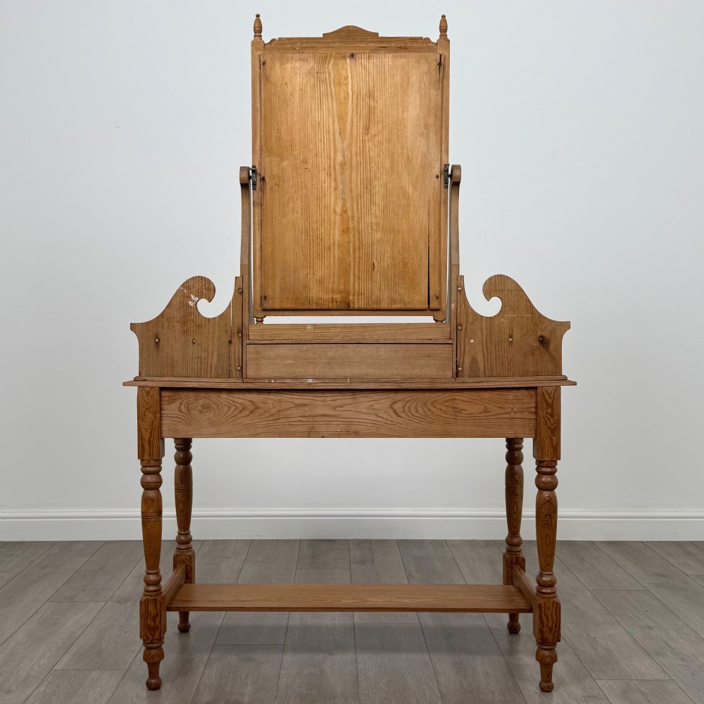 A Victorian pitch pine dressing table featuring a central swivel mirror, side scroll shelves, frieze drawers with brass handles, and turned legs with a low shelf. View V
