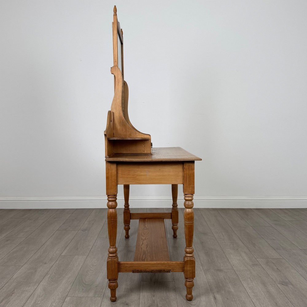 A Victorian pitch pine dressing table featuring a central swivel mirror, side scroll shelves, frieze drawers with brass handles, and turned legs with a low shelf. View VII