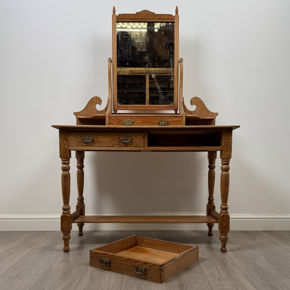 A Victorian pitch pine dressing table featuring a central swivel mirror, side scroll shelves, frieze drawers with brass handles, and turned legs with a low shelf. View X