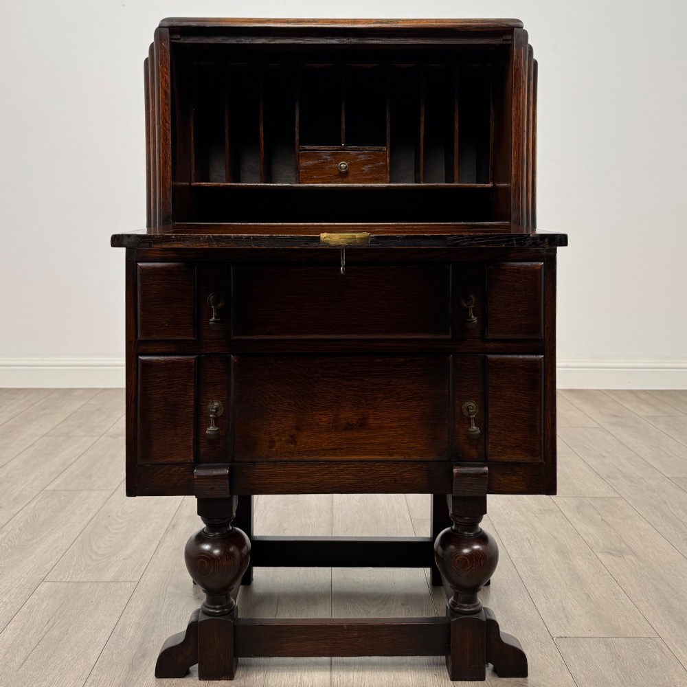 An early 20th-century dark oak writing bureau featuring a sloped fall-front lid above two drawers, supported on turned bulbous legs with stretchers. View II