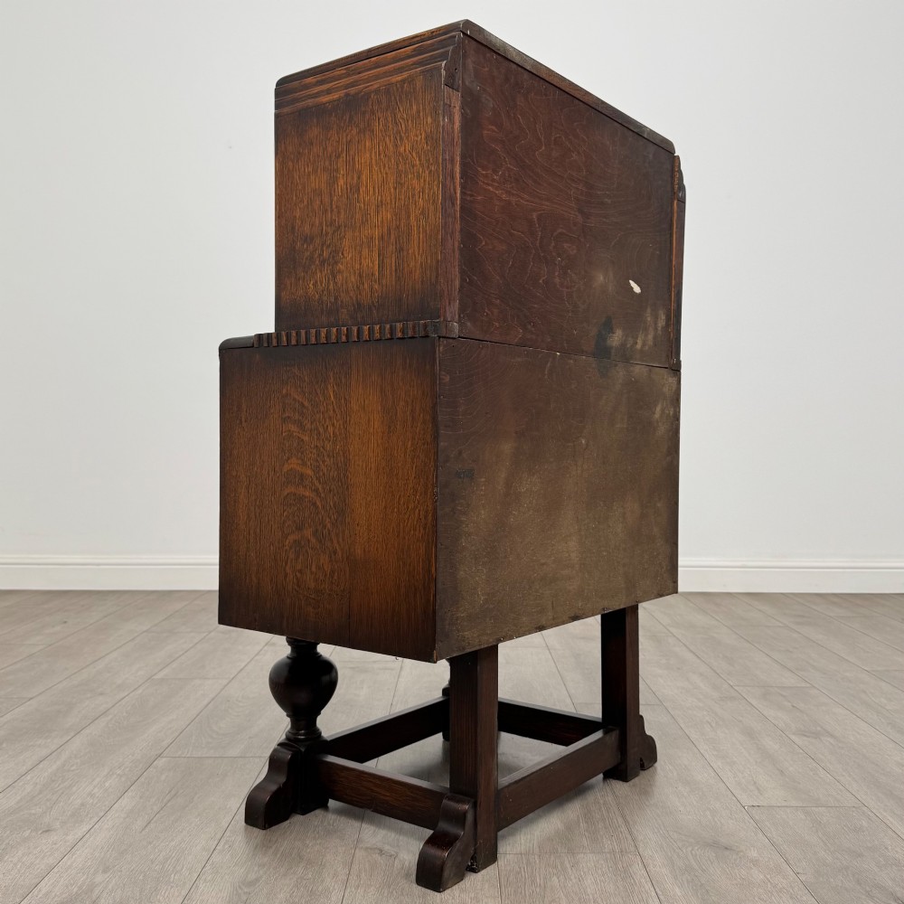 An early 20th-century dark oak writing bureau featuring a sloped fall-front lid above two drawers, supported on turned bulbous legs with stretchers. View V