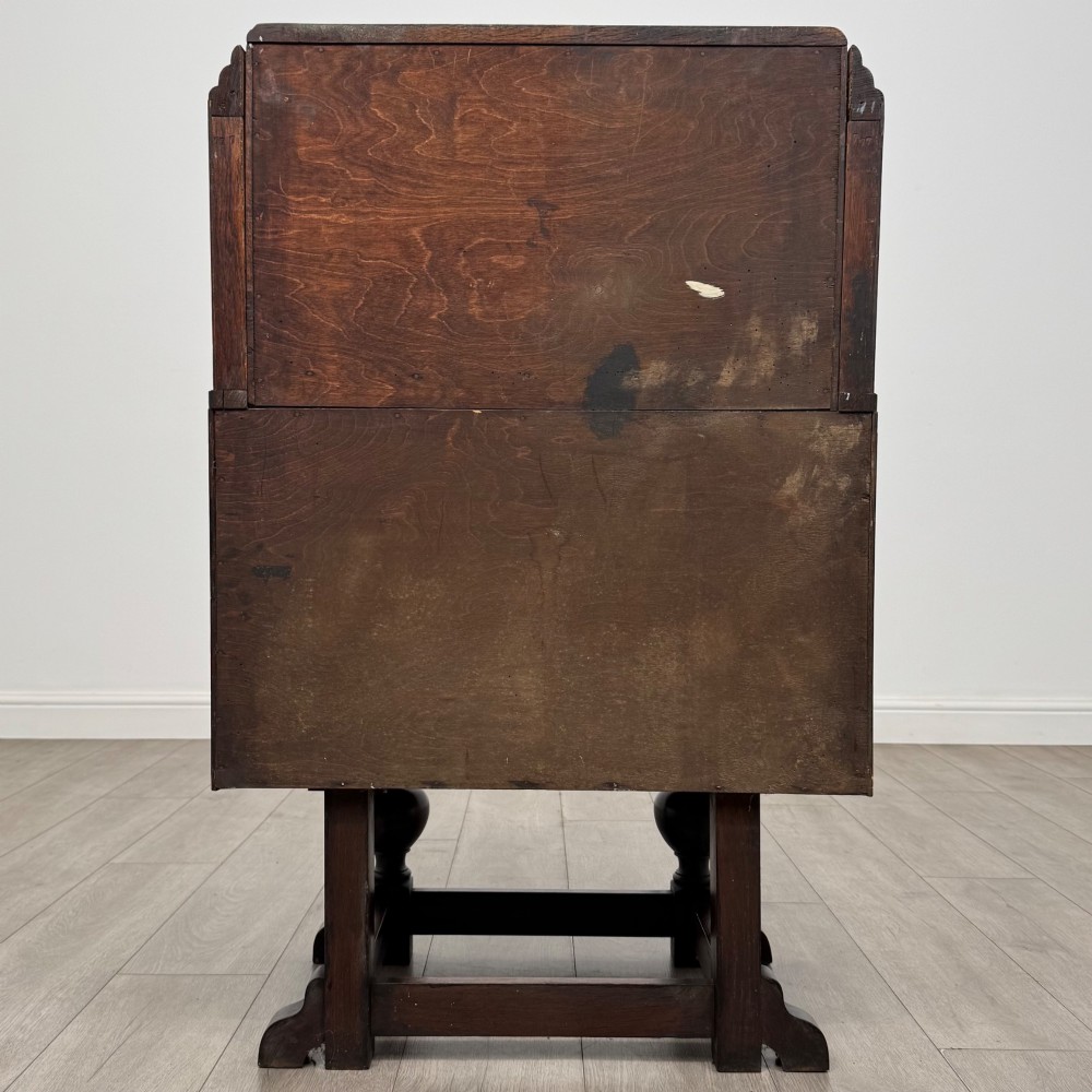 An early 20th-century dark oak writing bureau featuring a sloped fall-front lid above two drawers, supported on turned bulbous legs with stretchers. View VI