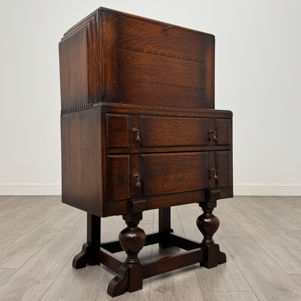 An early 20th-century dark oak writing bureau featuring a sloped fall-front lid above two drawers, supported on turned bulbous legs with stretchers. View IX