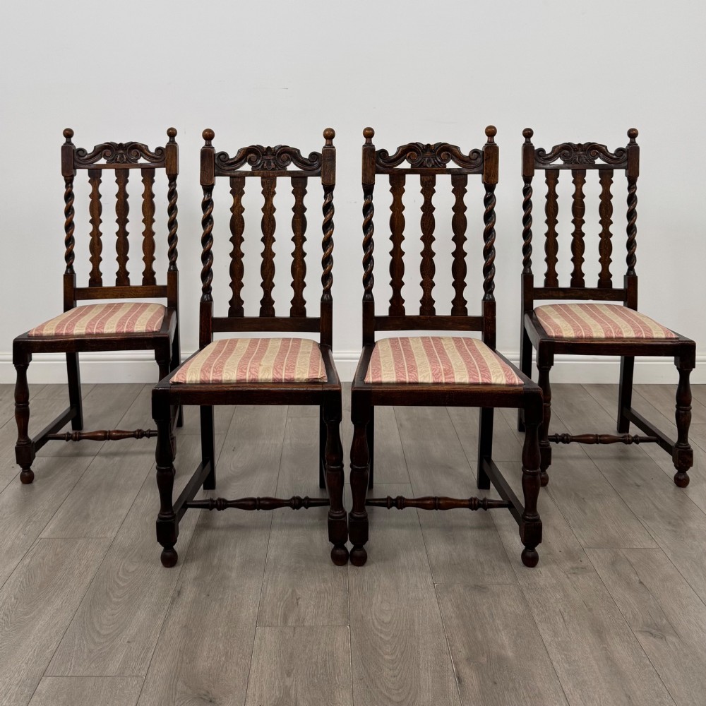 A set of four dark oak dining chairs with barley twist side supports, carved top crests, vertically slatted backrests, and striped fabric seat cushions.