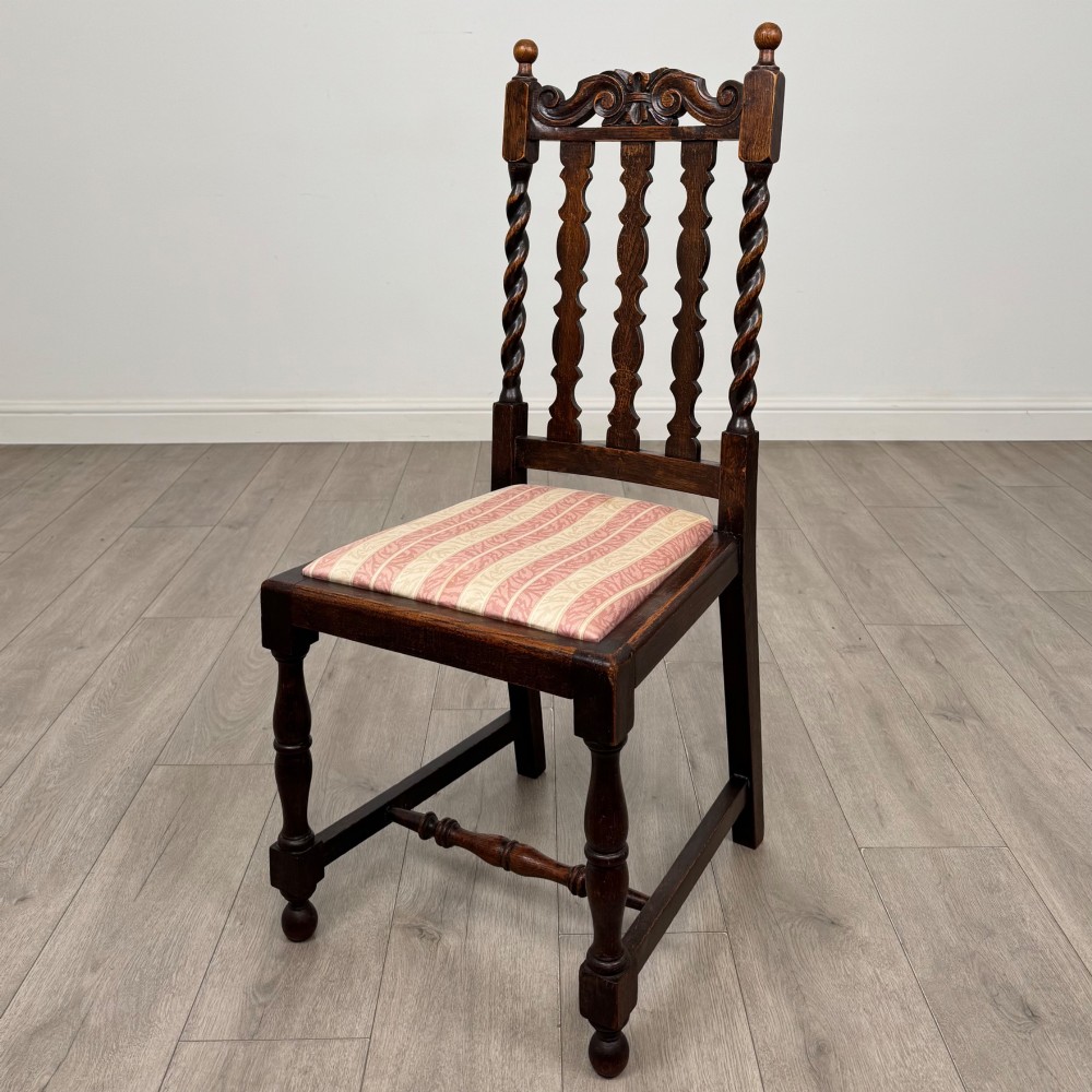 A set of four dark oak dining chairs with barley twist side supports, carved top crests, vertically slatted backrests, and striped fabric seat cushions. View II