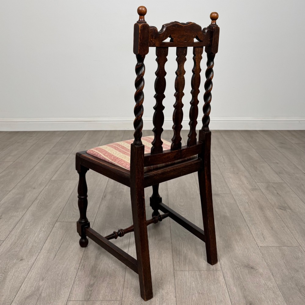 A set of four dark oak dining chairs with barley twist side supports, carved top crests, vertically slatted backrests, and striped fabric seat cushions. View III