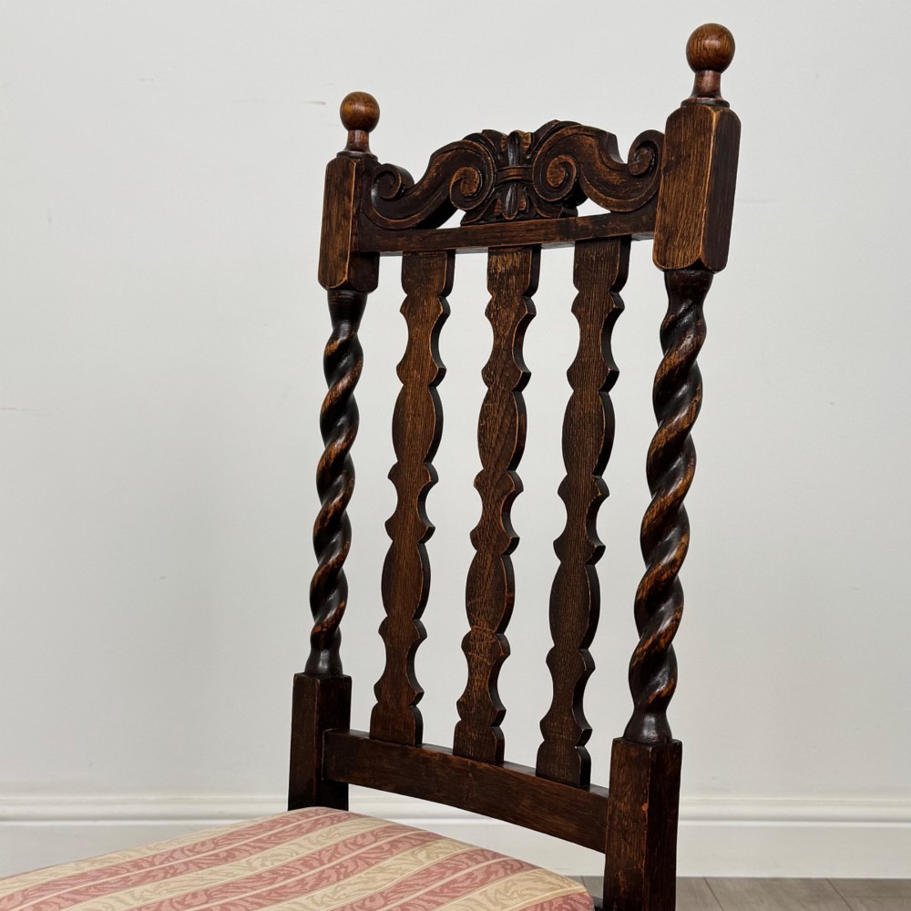 A set of four dark oak dining chairs with barley twist side supports, carved top crests, vertically slatted backrests, and striped fabric seat cushions. View IV